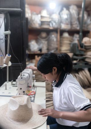 A young Hispanic woman is sewing a natural fiber hat