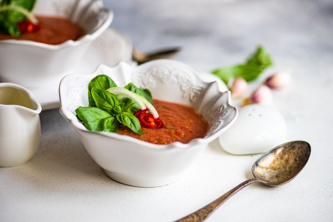 Bowls of gazpacho soup with basil, garlic, and salt and pepper shakers