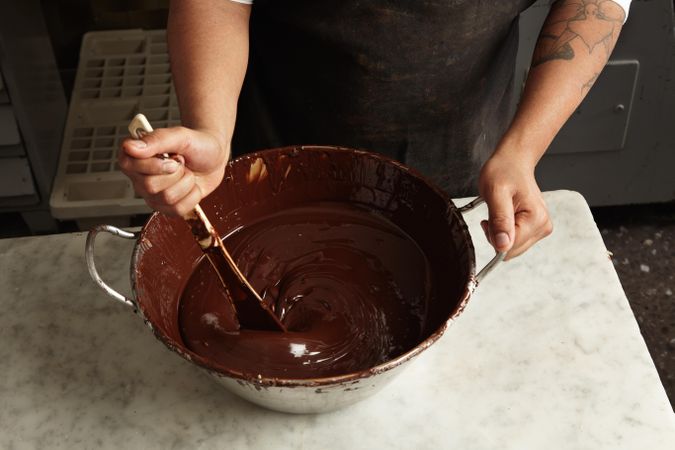 Top view of hands stirring melted chocolate with spatula