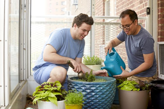 Two men water plant on their balcony