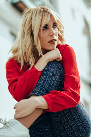 Blonde female with red shirt sitting with arms leaning on her knee, vertical