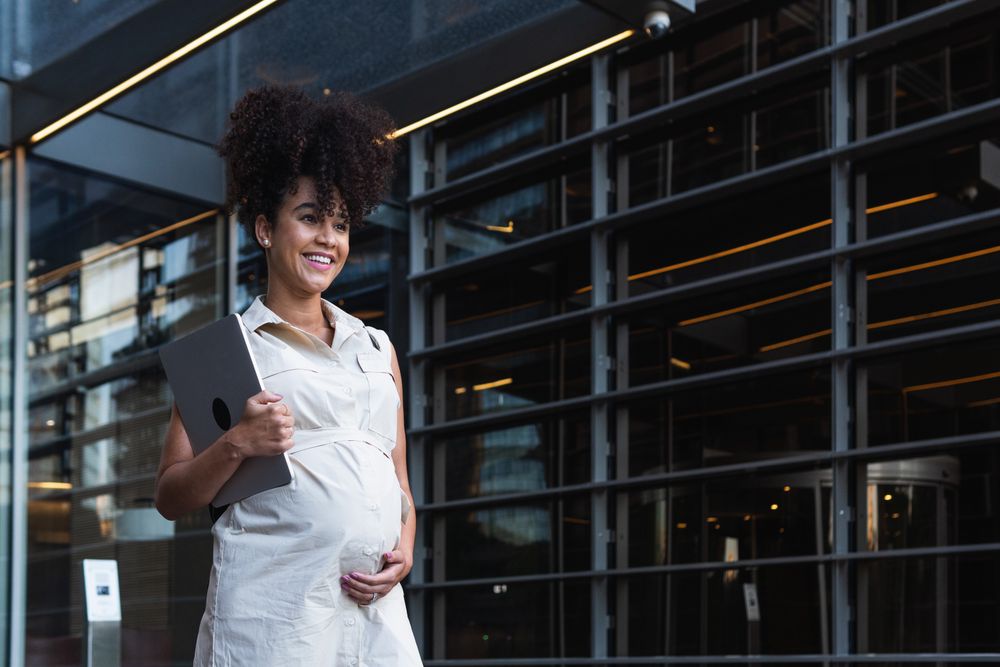 Smiling Black woman with laptop coming out of office building
