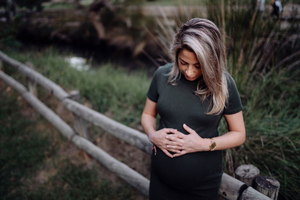 Happy pregnant woman standing at river in park