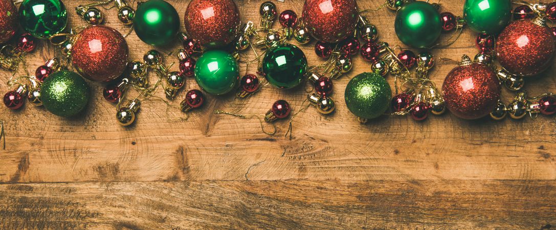 Tree ornaments on wooden background, red, green and gold baubles, wide composition, copy space