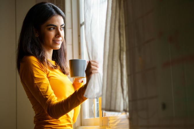 Woman gazing out the window with warm beverage
