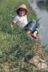 Smiling boy siting on grass near river