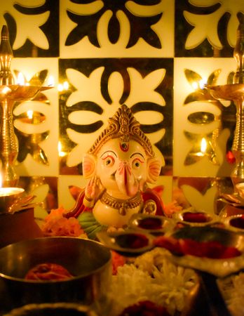 Ganesh figurine surrounded by lit diyas and flowers