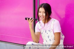 Smiling Chinese woman talking on cell phone sitting next to pink 5kAkGb