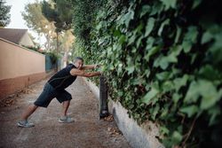 Mature man stretching on botanical wall in street