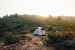 Man setting up a tent in a field with parked motorcycle