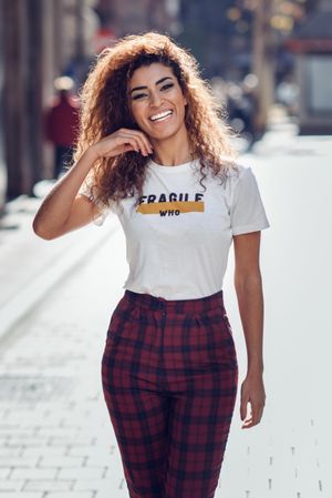 Smiling Arab woman with curly hair walking down sunny street