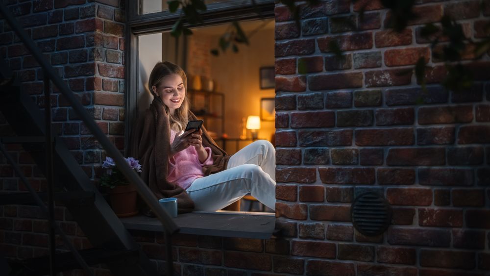 White Woman Using Smartphone While Sitting on an Open Windowsill.