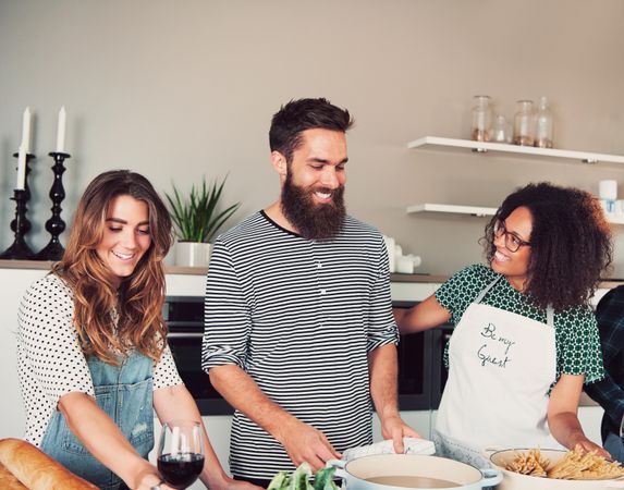 Group of smiling friends cooking pasta and drinking wine