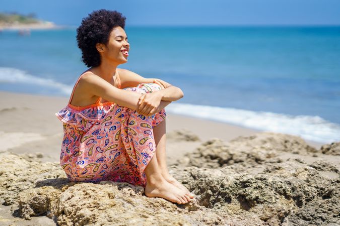 Smiling woman sitting on the rocks on the coast looking out to the sea