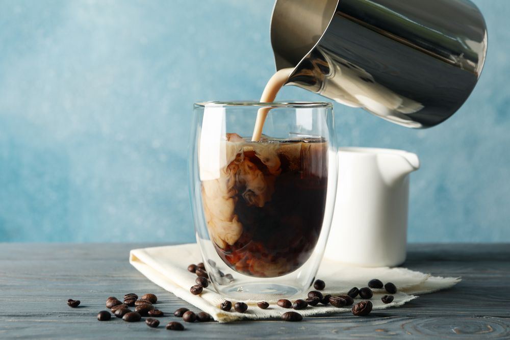 Milk is poured into a glass of coffee. Composition with ice coffee