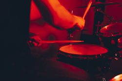 Anonymous man with drumsticks playing on drums in redness