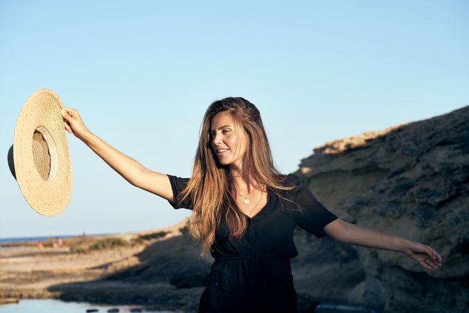 Cheerful woman holding hat in air