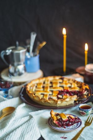 Homemade cherry pie on table with lit taper candles