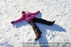 Child in pink snow suit lying in the snow making snow angel bYZEN0