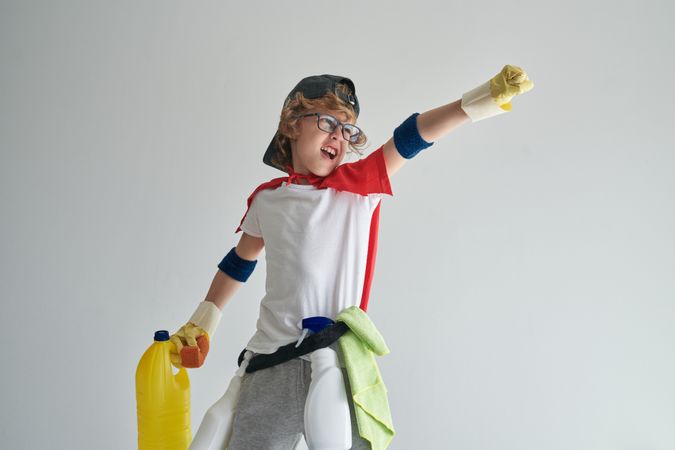 Funny boy in superhero costume standing with cleaning tools in s