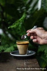 Cropped image of person holding a teaspoon over a cup of coffee 0gqjl4