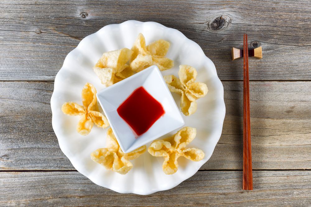 Fried wanton shells and sweet dipping sauce in bowl on rustic wood