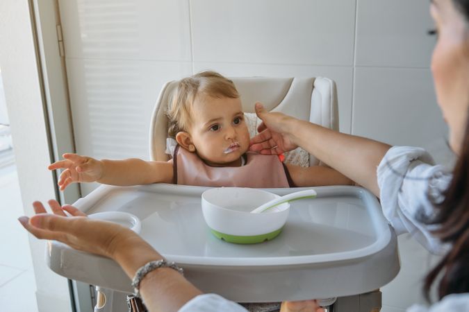 Baby girl sitting on high chair and looking at mother