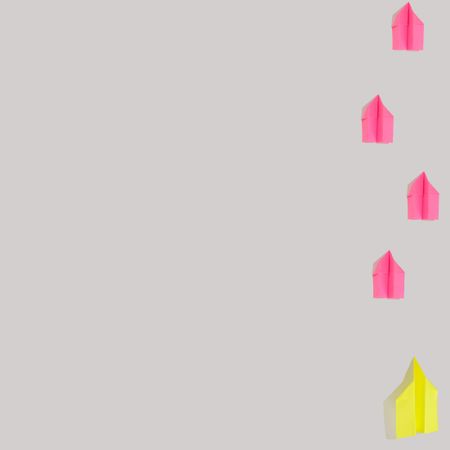 Flat lay of paper airplanes in pink and yellow flying up