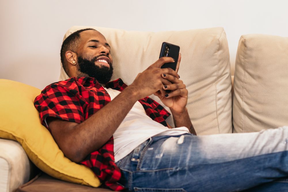 Black man relaxing using smartphone on the sofa at home