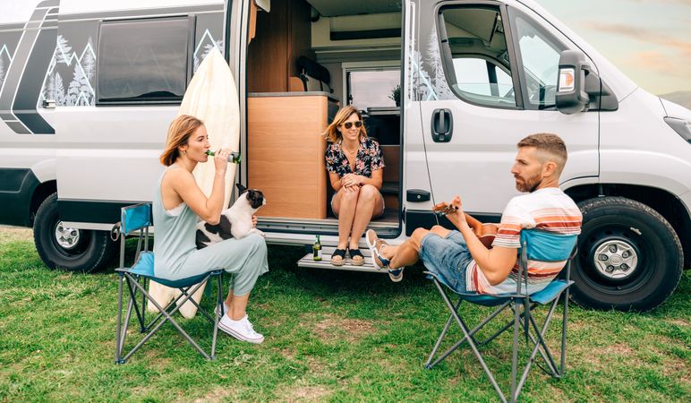 Three friends sitting outside a motorhome with beers, a ukulele and a dog