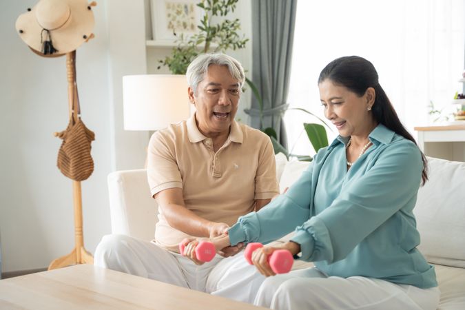 Asian mature couple exercise with lifting dumbbell for strength training at home