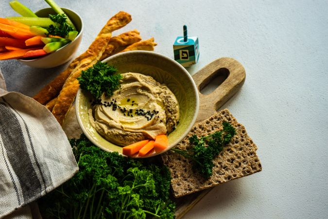 Traditional hummus dip in bowl on board served with veggies and crackers