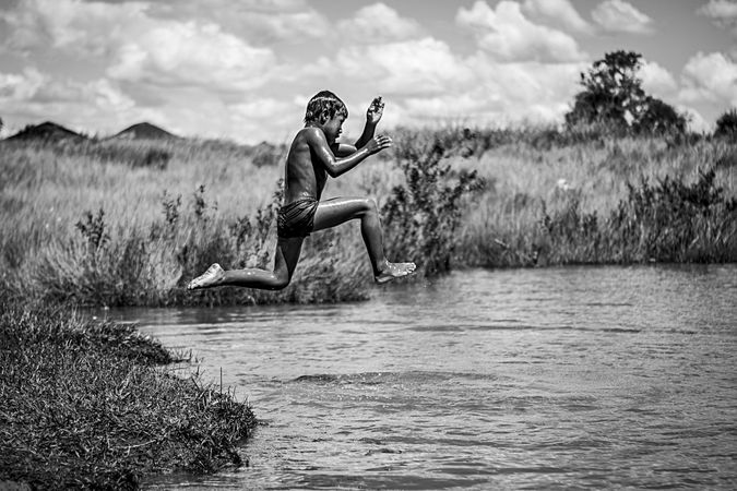 Grayscale photo of boy jumping on water