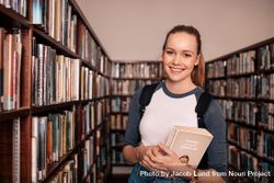 Young female student standing and holding book in university library 47JNB5