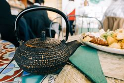 Teapot near plate with delicious food on table