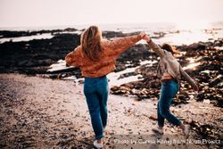 Two young women walking along the beach holding hands high Q4dAab