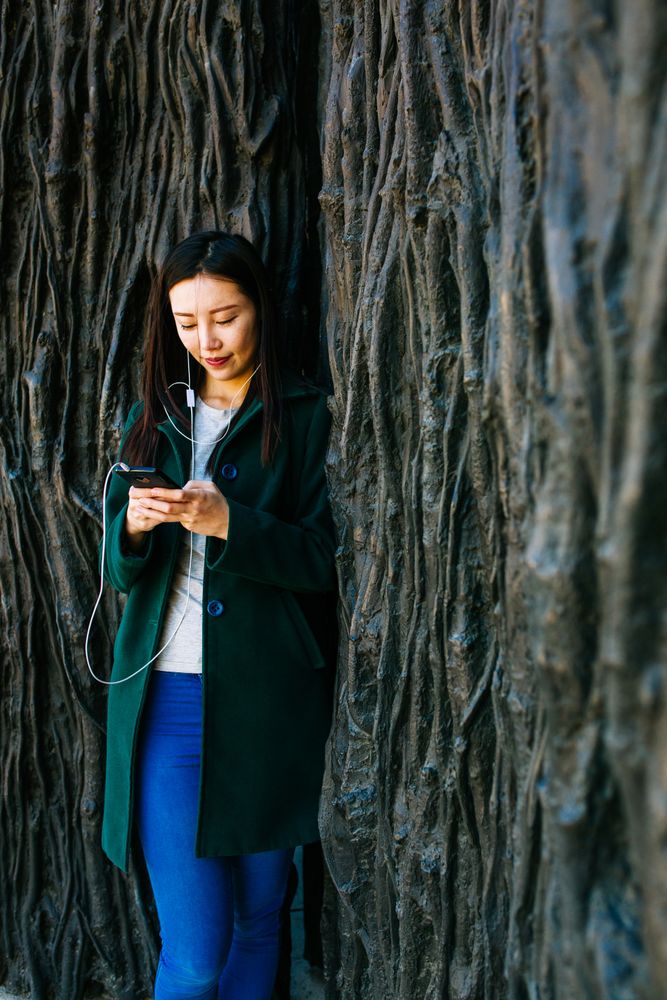 Asian female listening to music near rough wall