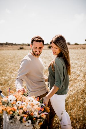 Sincere lovers posing by bicycle on rye field