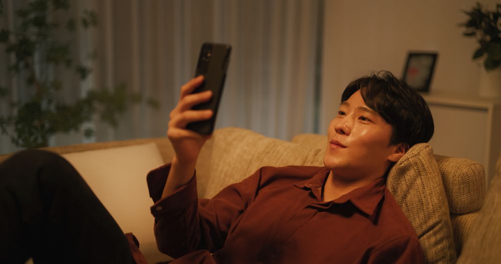 South Korean Young Man Enjoying His Leisure Time while Relaxing and Using a Smartphone.