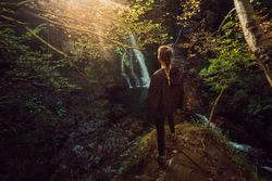 woman standing in a Small river and waterfall flowing in green dark beautiful forest.