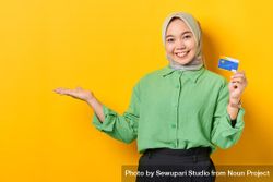 Muslim woman in headscarf and green blouse holding credit card with palm up on copy space 4AqBQ4