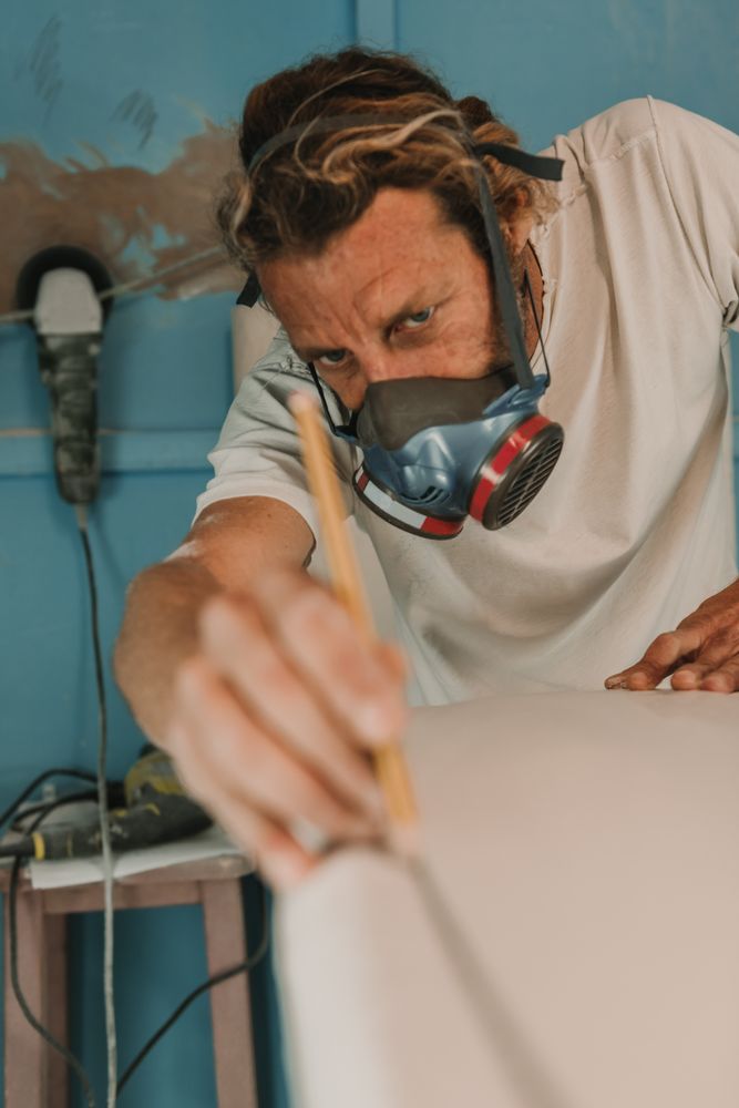 Man in respirator measuring surf board in workshop