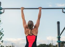 back view of a woman athlete doing pull ups on a bar outdoors, calisthenics