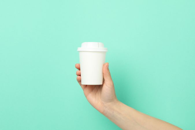 Female hand holds paper cup on mint background, space for text