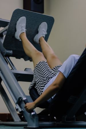 woman using leg press machine in fitness center wearing shoes and short skirt and pressing the machine with her legs.
