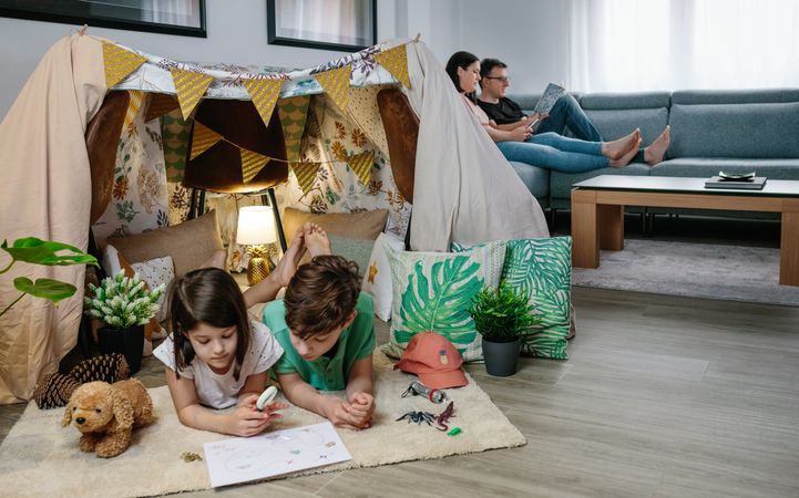 Children playing camping at home while their parents read and look at the mobile