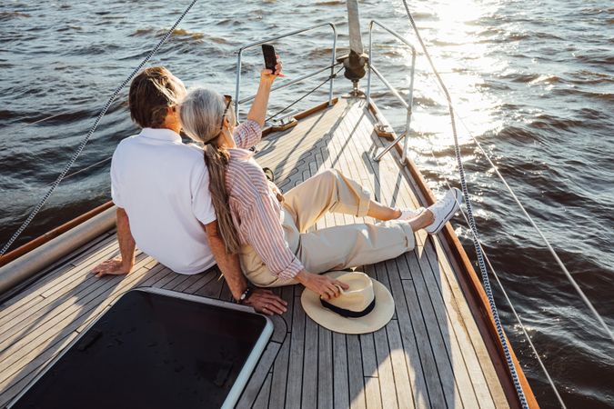 Two older people sitting together on a yacht bow and taking selfie