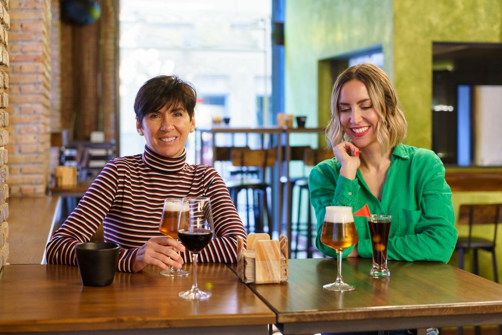 Two women smiling with drinks at counter of bar