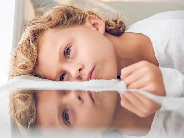 Dreamy boy lying on sofa and reflected in tablet screen