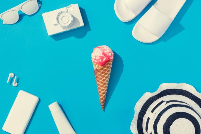 Summer objects of flip flops, sunglasses, camera, smart phone, hat and ice cream on blue background